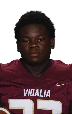 A person wearing a maroon football jersey with the number 33 and the word Vidalia is holding a football in one hand. Description generated by AI