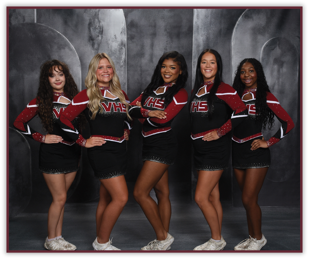 Five people wearing matching cheerleading uniforms with “VHS" on the front pose with hands on hips against a dark studio backdrop. Description generated by AI