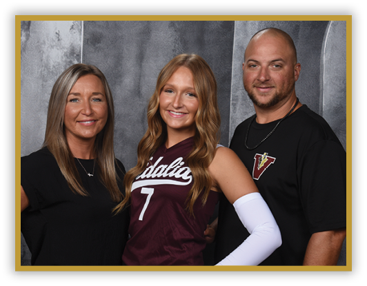Three adults stand closely together smiling, with one wearing a sports jersey and arm sleeve, and the others dressed in casual clothing against a gray backdrop. Description generated by AI