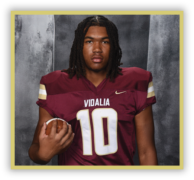 A person with shoulder-length dreadlocks wearing a maroon football jersey with the number 10 and the word Vidalia is holding a football. Description generated by AI