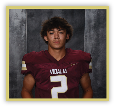 A person with medium-length tousled hair wearing a maroon football jersey with the word Vidalia and the number 2 stands against a dark textured background. Description generated by AI