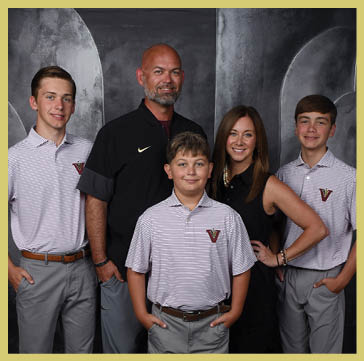 Five people wearing matching striped polo shirts and one person in a black shirt pose together against a dark, textured backdrop. Description generated by AI
