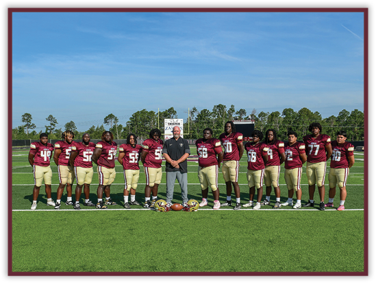 A group of people wearing maroon and gold football uniforms stand in a line on a football field with a coach in casual clothing standing in the center. Description generated by AI