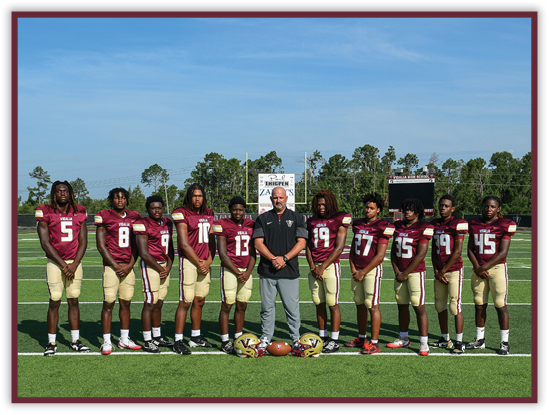 A group of people wearing maroon and gold football uniforms stand on a football field with a coach in the center holding a football. Description generated by AI