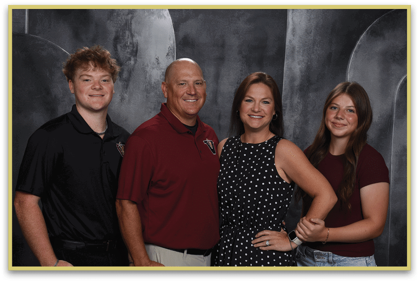 Four people stand closely together smiling against a dark backdrop, with two wearing polo shirts and the other two wearing casual tops. Description generated by AI
