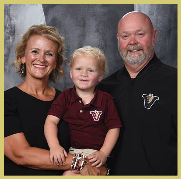 Five people wearing matching striped polo shirts and one person in a black shirt pose together against a dark, textured backdrop. Description generated by AI