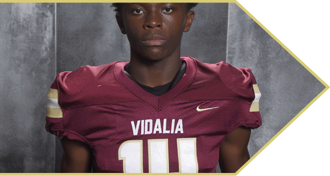 A person wearing a maroon sports jersey with white and gold lettering is shown from the shoulder to mid-torso. Description generated by AI