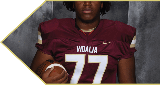 A person wearing a maroon sports jersey with white and gold lettering is shown from the neck down. Description generated by AI