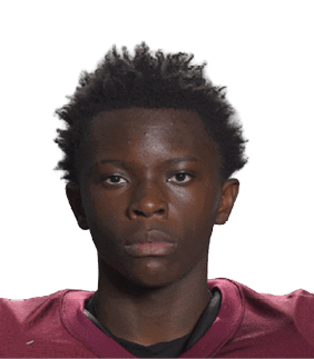 A person wearing a maroon football jersey with the number 14 and the word Vidalia is holding a football in front of a white background. Description generated by AI