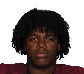 Person wearing a maroon football jersey with the number 77 and beige pants is holding a football. Description generated by AI