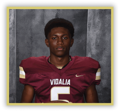 A person wearing a maroon football jersey with the word Vidalia and the number 5 stands against a gray textured backdrop. Description generated by AI