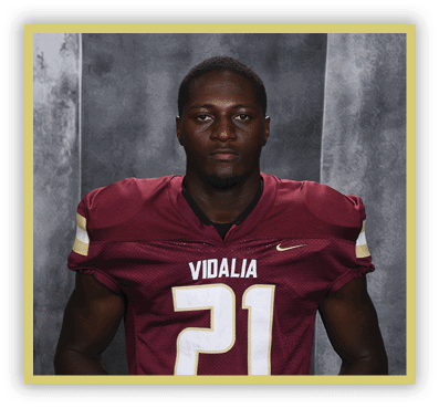 A person wearing a maroon football jersey with the number 21 and the word Vidalia stands against a gray textured background. Description generated by AI