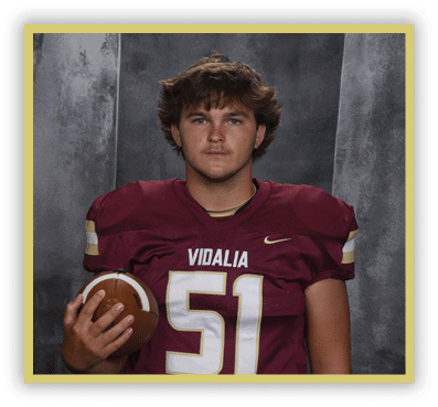 A person with long dreadlocks wearing a maroon football jersey with the number five and the word Vidalia is holding a football against a gray textured background. Description generated by AI