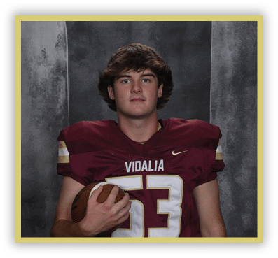 A person with medium-length hair wearing a maroon football jersey with the number 53 and the word Vidalia is holding a football against a dark textured background. Description generated by AI