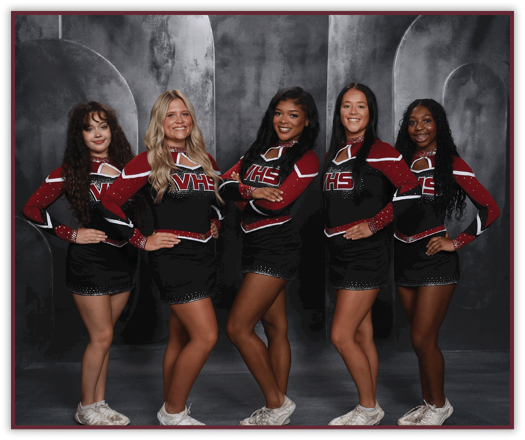 Five people wearing matching cheerleading uniforms with “VHS" on the front pose with hands on hips against a dark studio backdrop. Description generated by AI