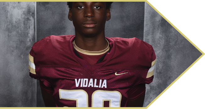 A person wearing a maroon football jersey with the word “VIDALIA" and the number 20 stands against a gray background. Description generated by AI