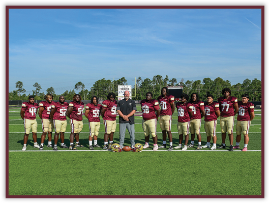 A group of people wearing maroon and gold football uniforms stand in a line on a football field with a coach in casual clothing standing in the center. Description generated by AI
