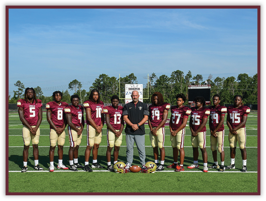 A group of people wearing maroon and gold football uniforms stand on a football field with a coach in the center holding a football. Description generated by AI