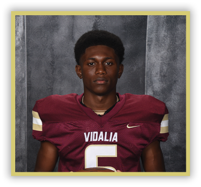 A person wearing a maroon football jersey with the word Vidalia and the number 5 stands against a gray textured backdrop. Description generated by AI