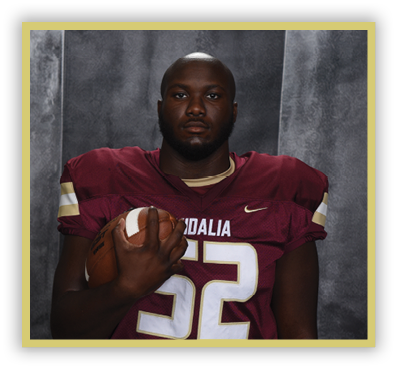 A person wearing a maroon football jersey with the word Vidalia and the number 5 stands against a gray textured backdrop. Description generated by AI