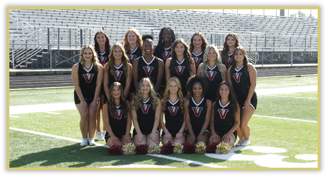 A group of people wearing matching black athletic uniforms with a red and white “V" logo pose together on a sports field with bleachers in the background. Description generated by AI