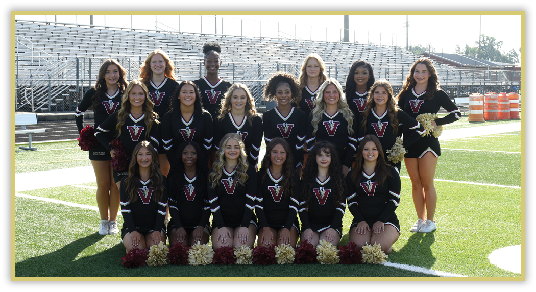 A group of adults in matching black cheerleading uniforms with a red and white logo pose on a football field with pom-poms arranged in front of them. Description generated by AI