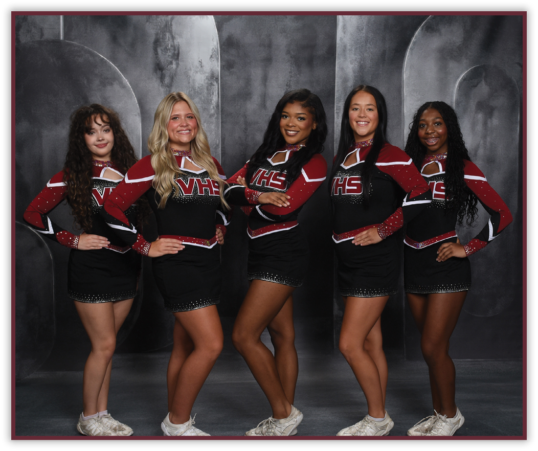 Five people wearing matching cheerleading uniforms with “VHS" on the front pose with hands on hips against a dark studio backdrop. Description generated by AI