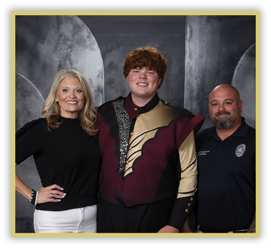Three people stand together smiling, with one person in the center wearing a decorative maroon and gold uniform, flanked by two others in casual and professional attire against a dark backdrop. Description generated by AI