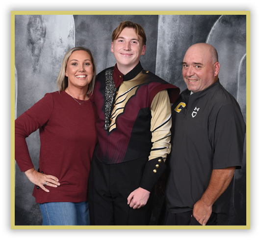 Three adults stand closely together smiling, with one wearing a maroon and gold uniform and the others dressed casually against a gray backdrop. Description generated by AI