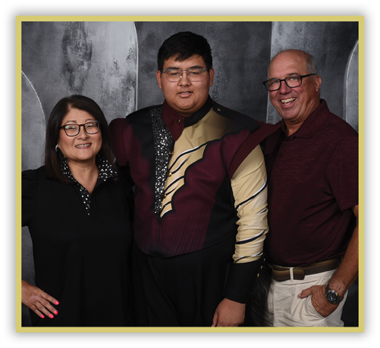 Three adults stand closely together smiling against a dark textured backdrop, with the person in the center wearing a maroon and gold uniform. Description generated by AI