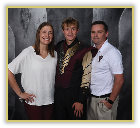 Three adults stand closely together smiling, with one wearing a marching band uniform and the others dressed in casual and semi-casual clothing against a dark backdrop. Description generated by AI