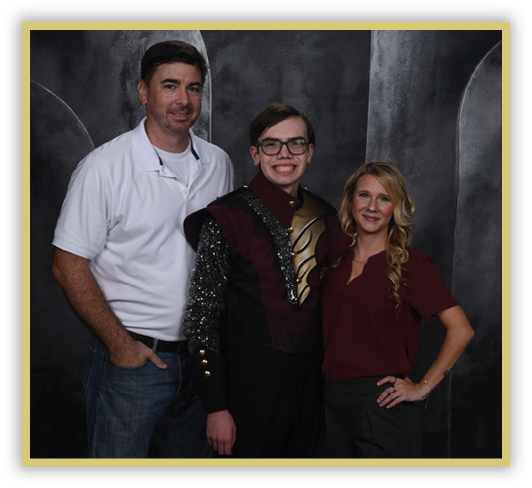 Three people stand closely together smiling, with one person in the center wearing a decorative uniform and the other two dressed casually against a dark backdrop. Description generated by AI