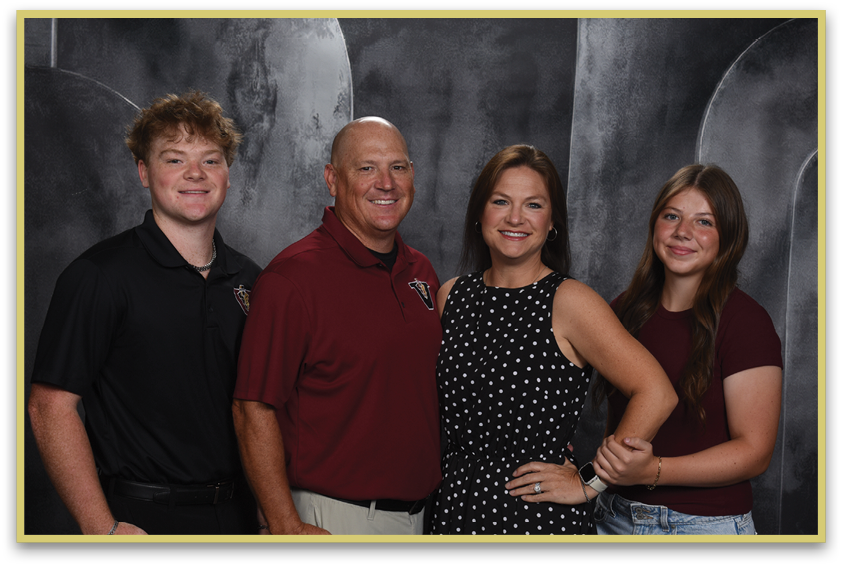 Four people stand closely together smiling against a dark backdrop, with two wearing polo shirts and the other two wearing casual tops. Description generated by AI