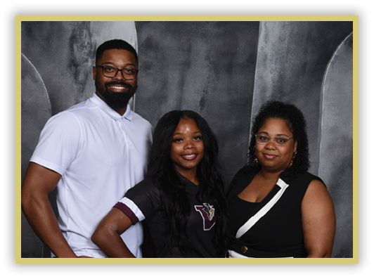 Three adults stand closely together smiling against a dark textured backdrop, with one wearing a white polo shirt, another in a black shirt with a logo, and the third in a black sleeveless top with glasses. Description generated by AI