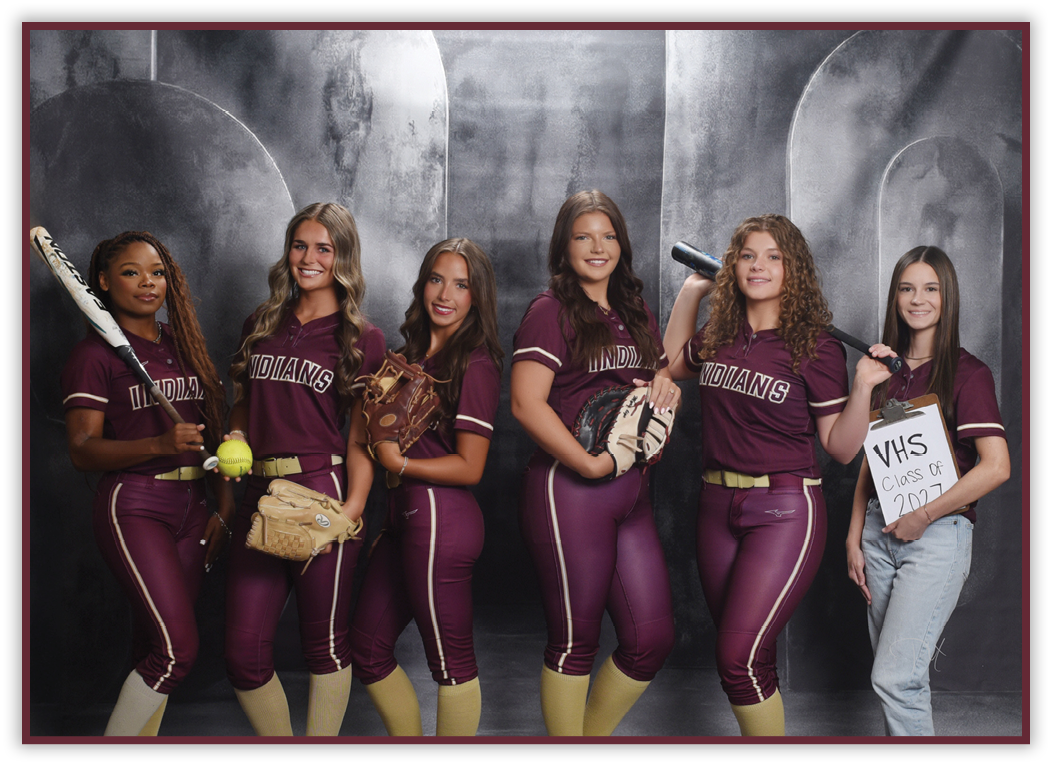 Six people wearing matching maroon softball uniforms and holding softball equipment pose together in front of a gray backdrop, with one person holding a sign that reads “VHS Class of 2024." Description generated by AI