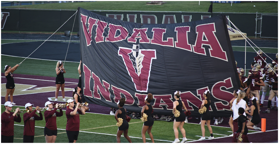 People in athletic uniforms and cheerleading outfits are holding a large banner with the words “VIDALIA INDIANS" on a sports field. Description generated by AI