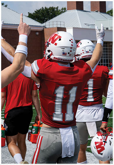 A group of people wearing red sports jerseys are sitting closely together, with one person in the center looking down thoughtfully. Description generated by AI