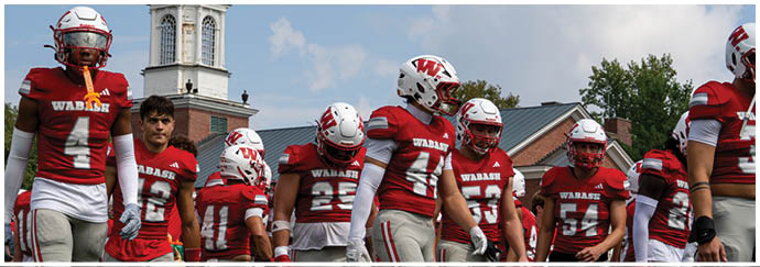 People in red football uniforms are walking out of a stadium entrance labeled “Little Giant Stadium" with a crowd of spectators in the background. Description generated by AI