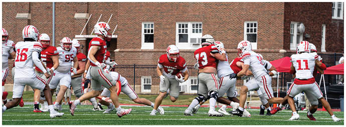 A group of people wearing white helmets with red “W" logos and red sports uniforms are huddled together on a green field. Description generated by AI