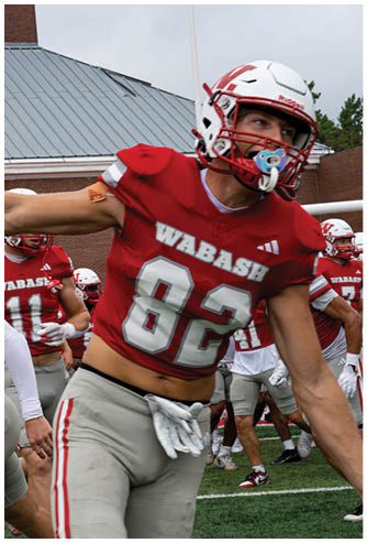 A person wearing a red football uniform with the number 8 on the back is standing on a football field with other players and spectators in the background. Description generated by AI