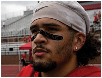 A person wearing a red football uniform with the word WABASH and the number 6 is crouched down against a partly cloudy sky. Description generated by AI