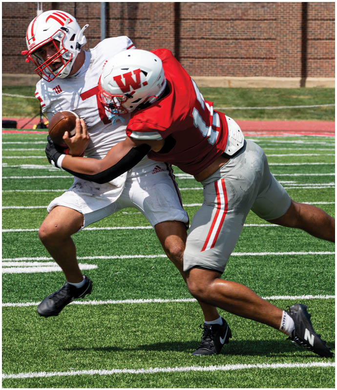 Two people in football uniforms are engaged in a tackle on a grassy field during a game. Description generated by AI