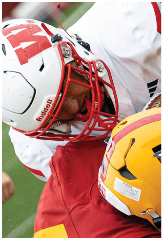 A person wearing a red football uniform with the number 8 on the back is standing on a football field with other players and spectators in the background. Description generated by AI