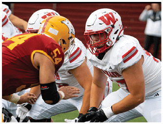 A person wearing a red football uniform with the word WABASH and the number 6 is crouched down against a partly cloudy sky. Description generated by AI