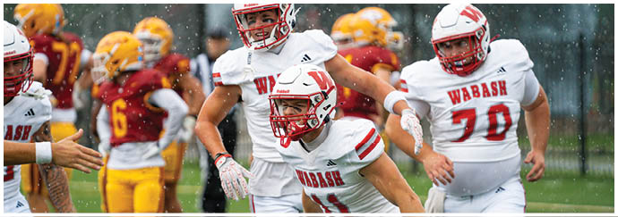 A person wearing a red football uniform with the number seven stands on a field with a crowd of people in the background and another person in a white football uniform nearby. Description generated by AI