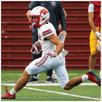 A group of people wearing red and white football uniforms are actively engaged in a game on a grassy field with one person holding a football tightly while others attempt to block or tackle. Description generated by AI