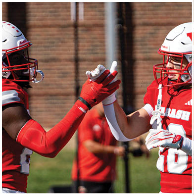 Four people in football uniforms are on a field with one person holding a football while others are attempting to tackle or block. Description generated by AI