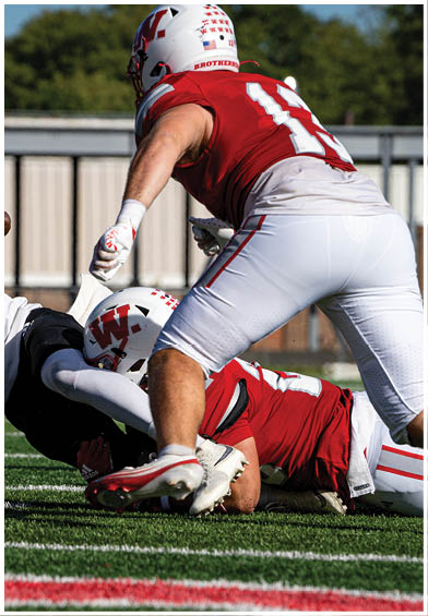 A group of people wearing red sports jerseys are sitting closely together, with one person in the center looking down thoughtfully. Description generated by AI