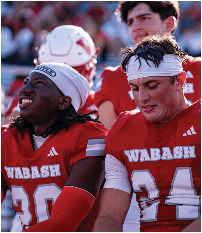 A person in a red football uniform tackles another person in a white football uniform who is holding a football on a green field during a game. Description generated by AI