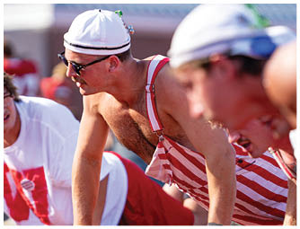 A person wearing a red football uniform with the word WABASH and the number 6 is crouched down against a partly cloudy sky. Description generated by AI